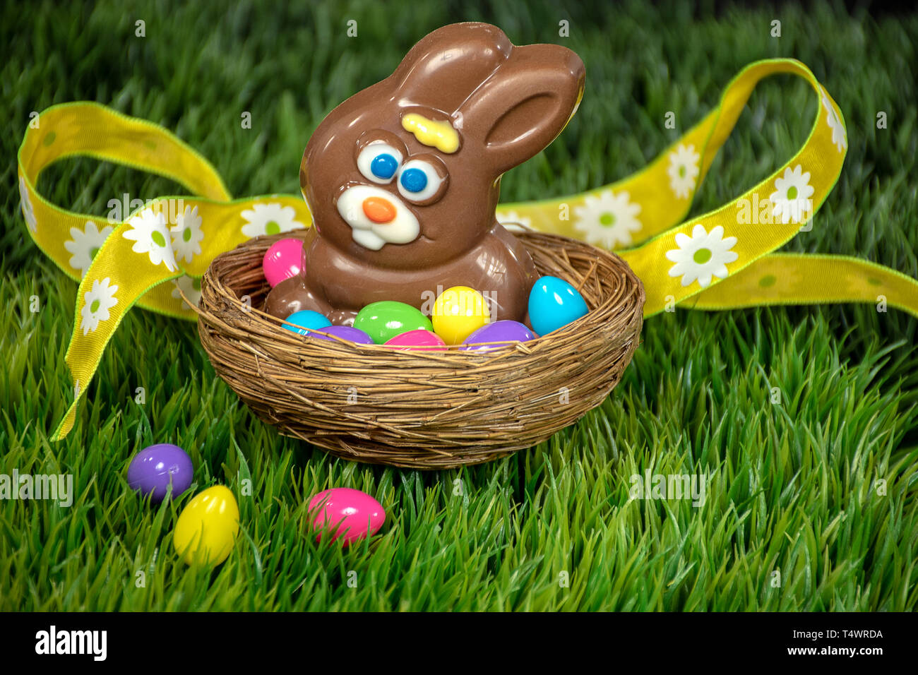 chocolate Easter rabbit in bird nest with colorful eggs on green grass and yellow ribbon Stock Photo