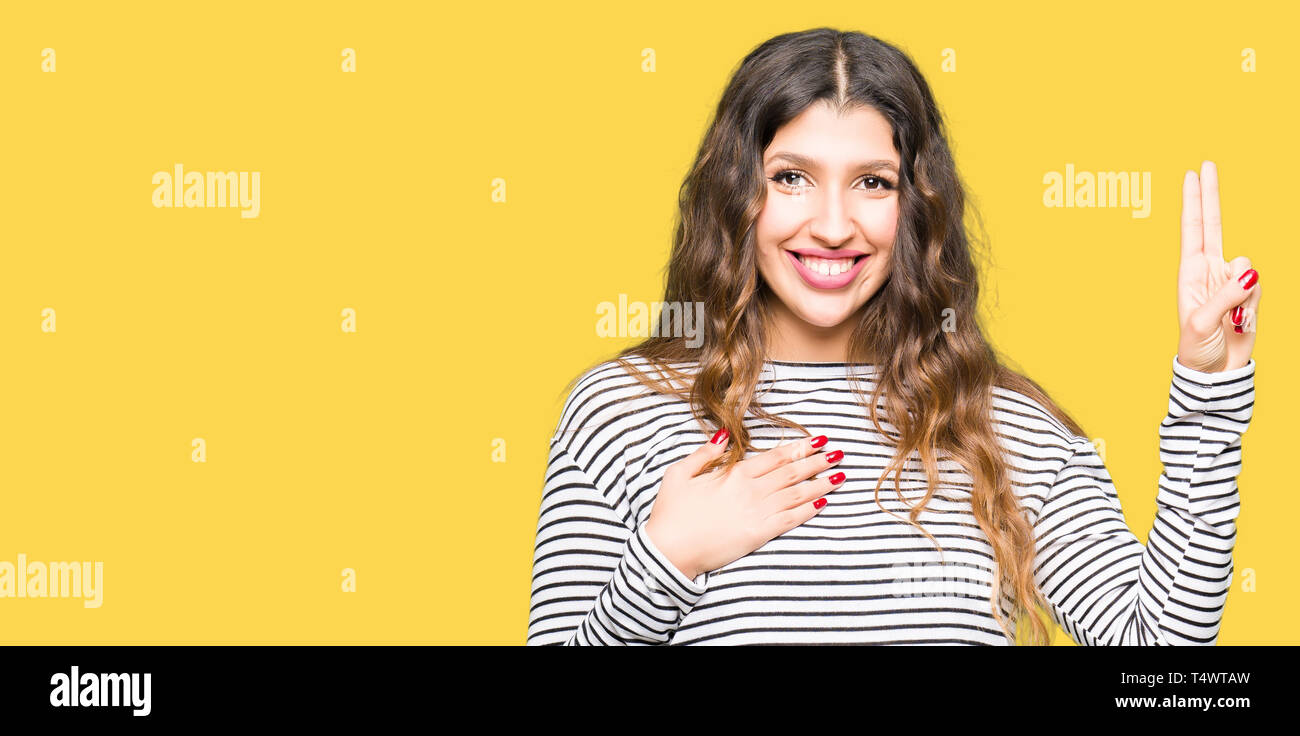 Young beautiful woman wearing stripes sweater Swearing with hand on chest and fingers, making a loyalty promise oath Stock Photo