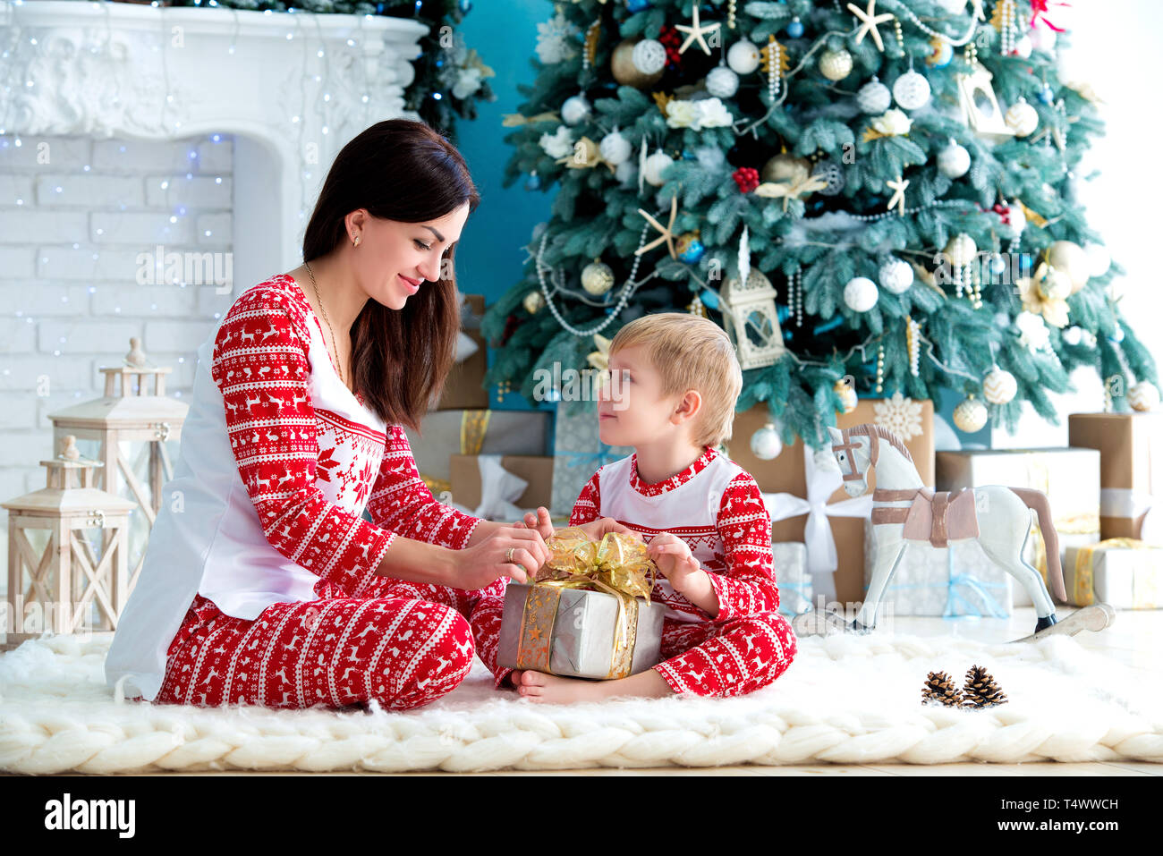 A young mother and son playing near the Christmas tree. Family in Christmas pajamas. Christmas homeliness. Holidays and New Year's gifts Stock Photo