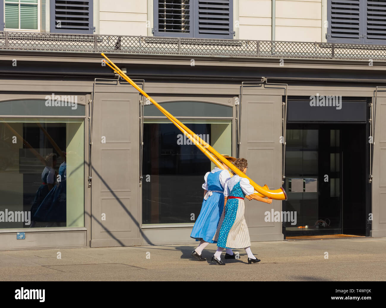 Zurich, Switzerland - August 1, 2018: two ladies carrying alpine horns passing along a street in the old town of city of Zurich to participate in the  Stock Photo