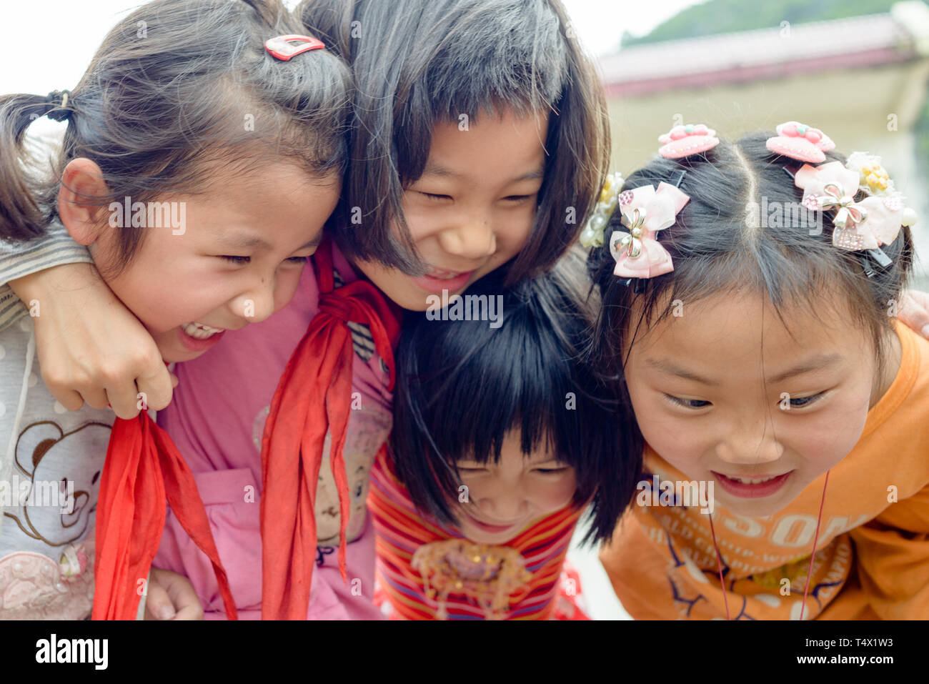 Four primary age school girls in group hug, laughing and shouting. Guangxi region, central southern China. Stock Photo