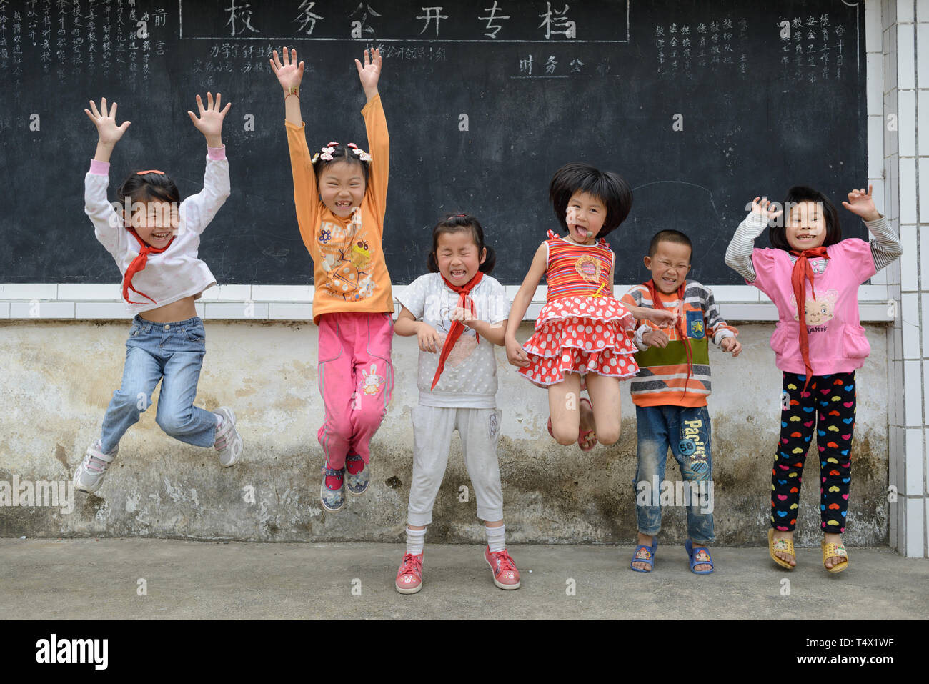 Primary age school children jumping and laughing in the school playground in rural Guangxi region, central southern China. Stock Photo