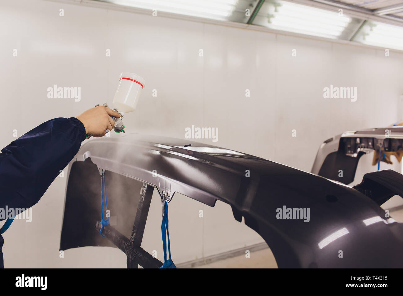 worker painting a car black blank parts in special garage, wearing
