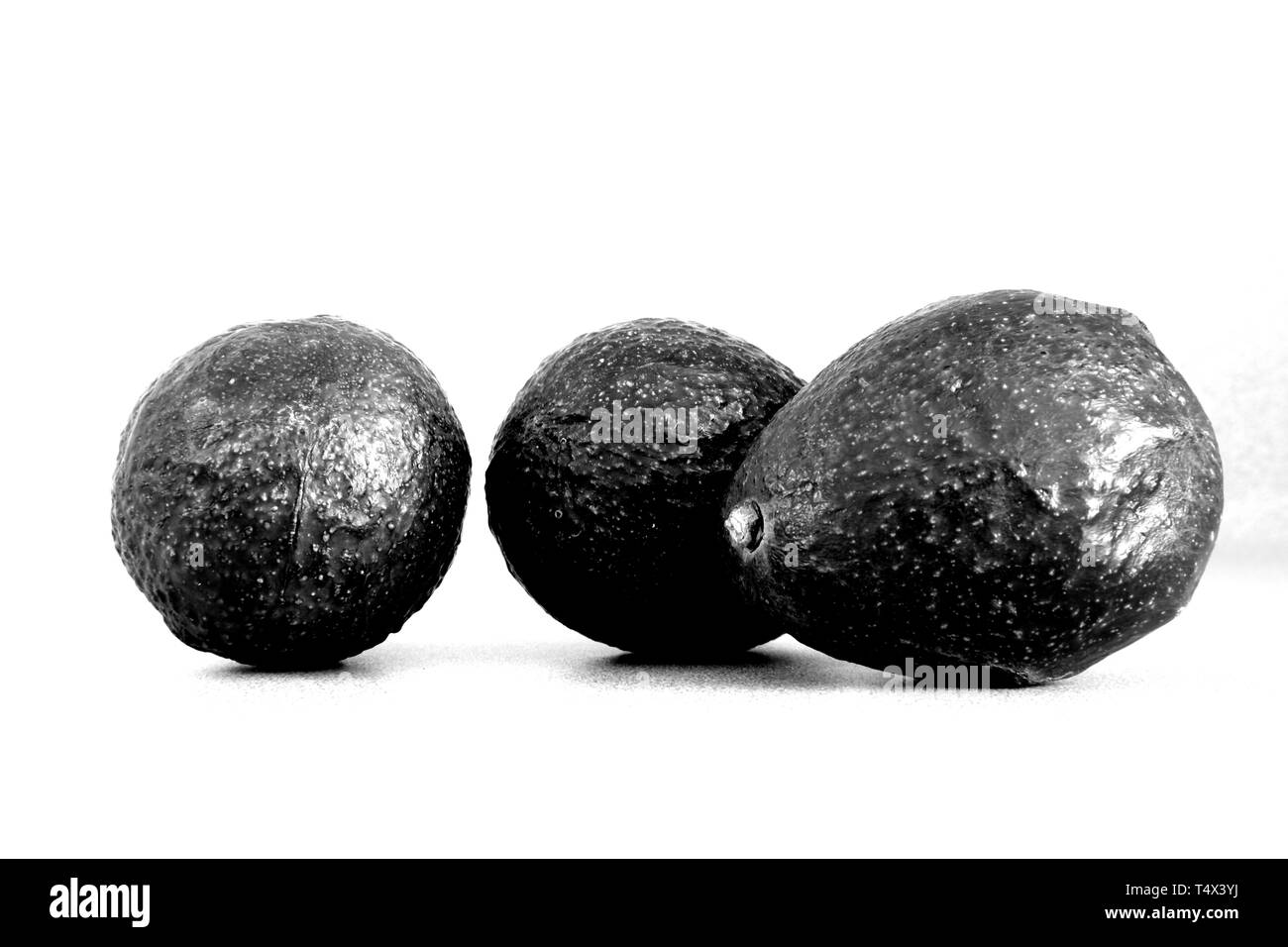 Three avocados (persea americana) on a light colored surface; avocado