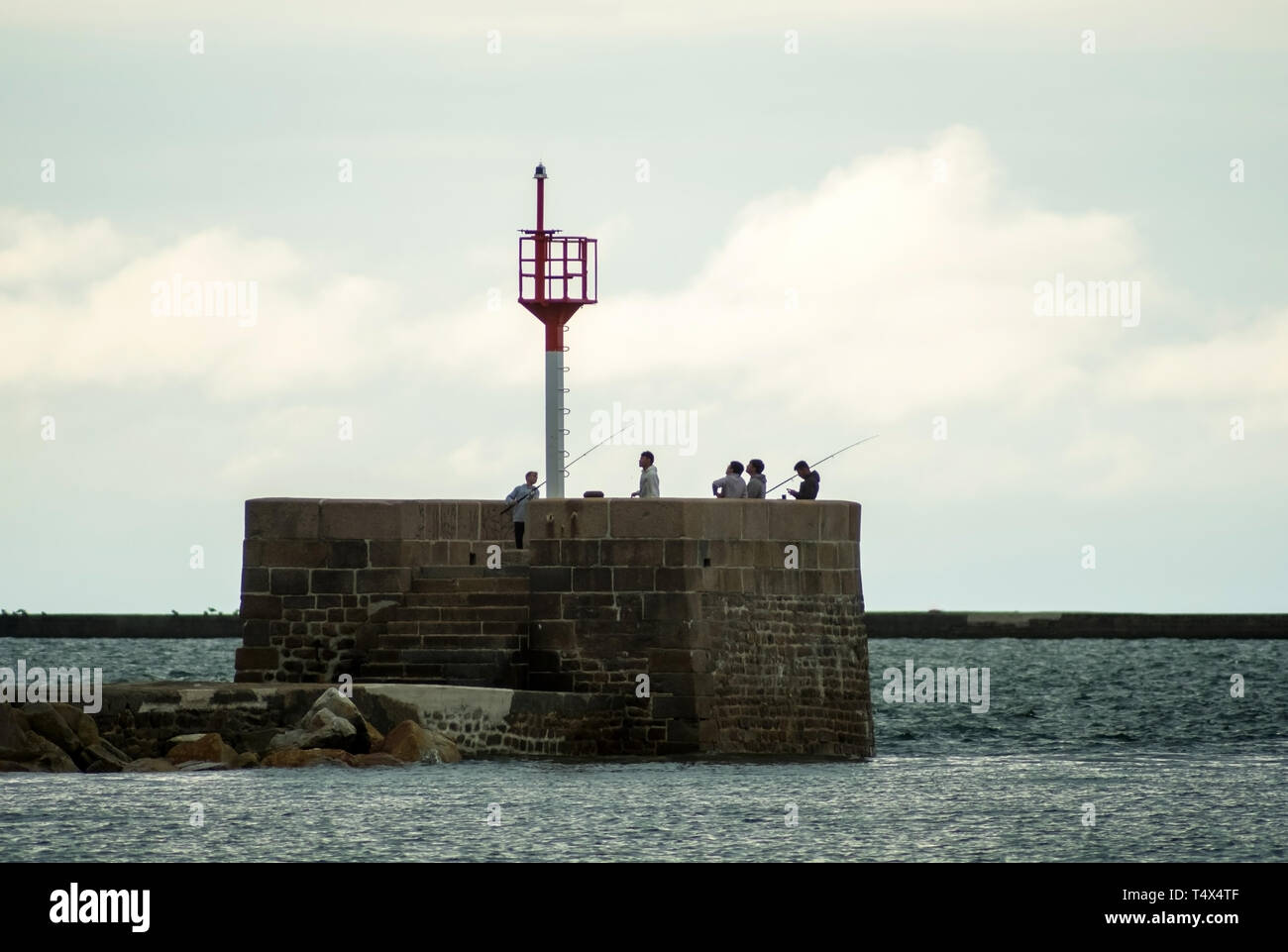 Cherbourg-Octeville, France - August 22, 2018: Lighthouse and fishermen in the harbor of Cherbourg during sunset. Normandy, France Stock Photo