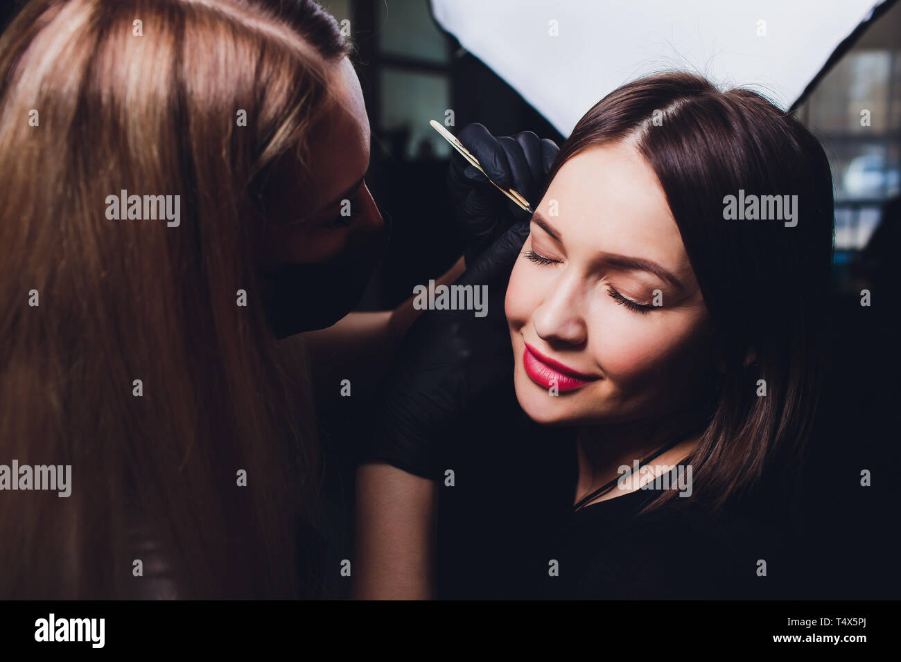 Cosmetologist making eyebrows design. Attractive woman getting facial care at beauty salon