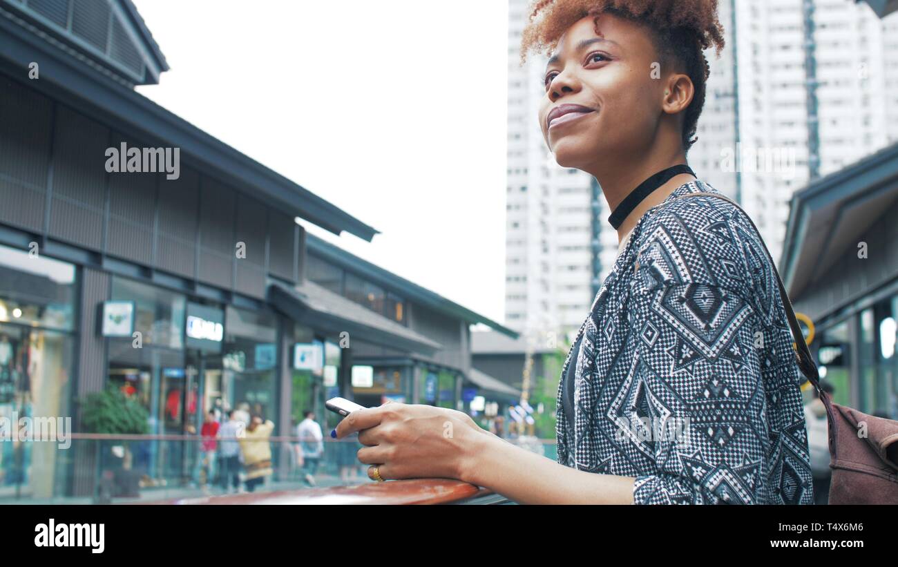 side view of happy young African woman using mobile phone in the street ...