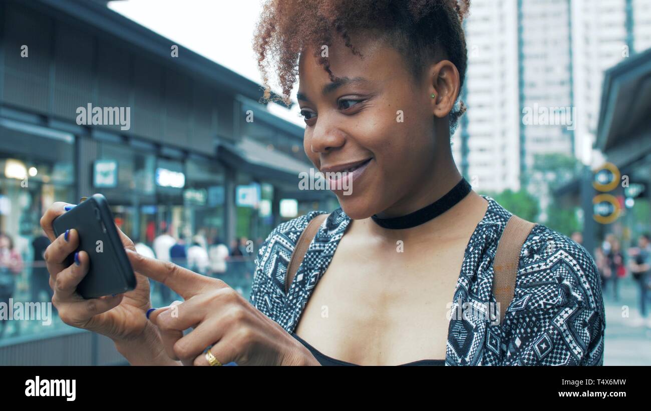 side view of happy young African woman using mobile phone in the street ...