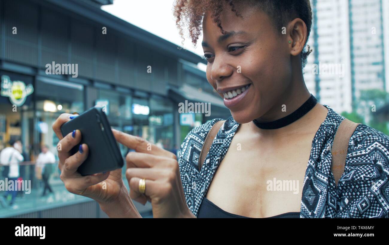 side view of happy young African woman using mobile phone in the street ...