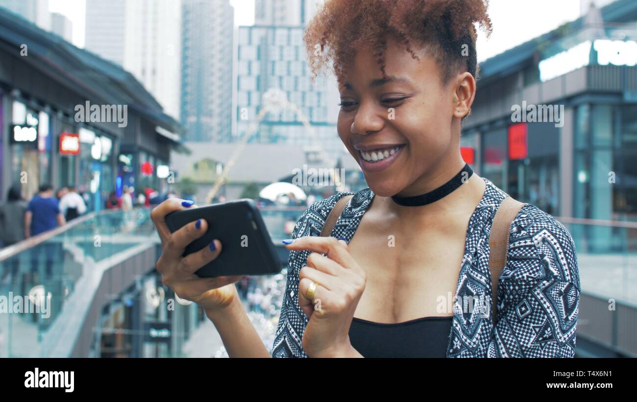 side view of happy young African woman using mobile phone in the street ...