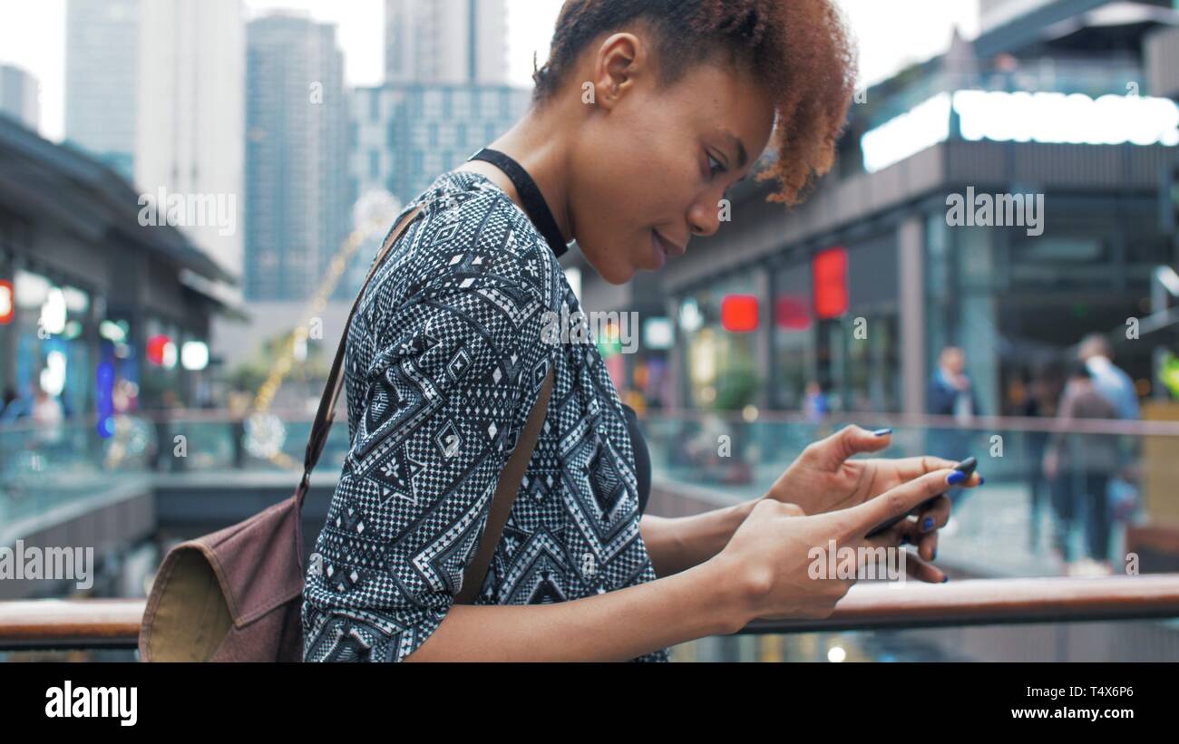 side view of happy young African woman using mobile phone in the street ...