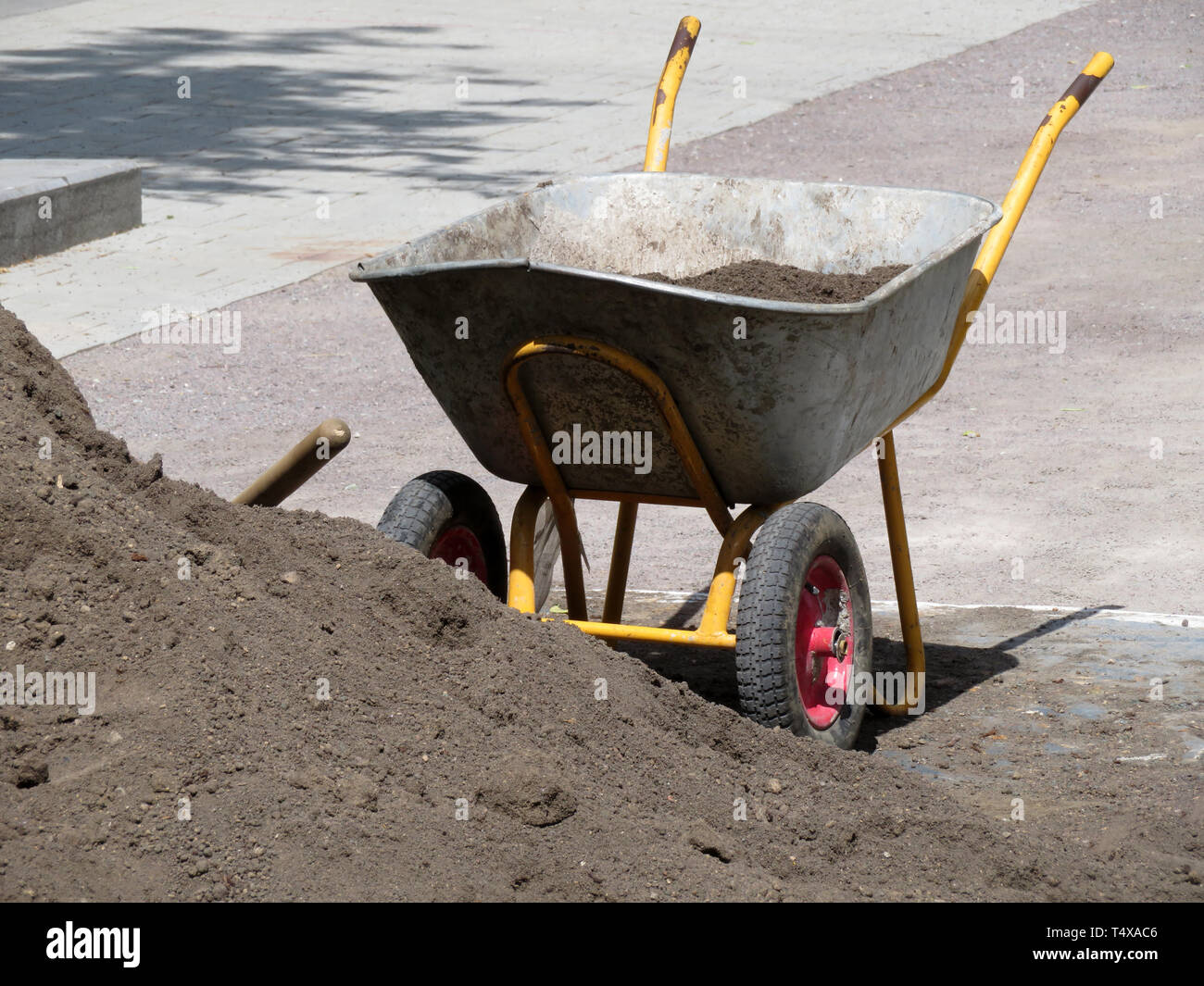 Metal wheelbarrow with the ground near the heap of soil. Earthworks, urban landscaping, laying of underground utilities Stock Photo