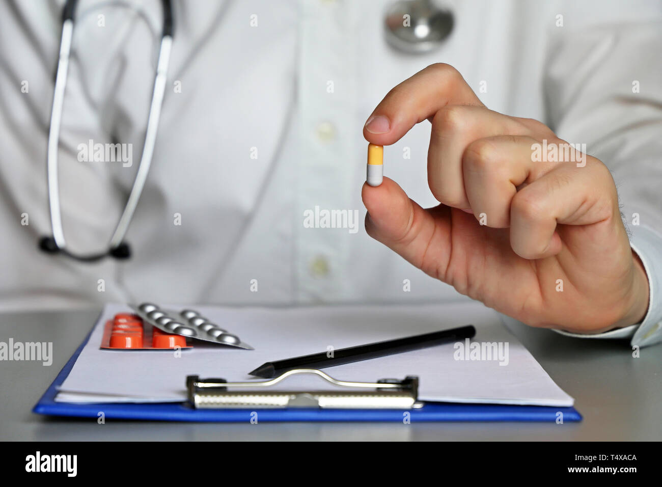 Doctor sitting in hospital office with pill in hand, physician at work giving medication in capsule. Concept of health care, medical appointment Stock Photo