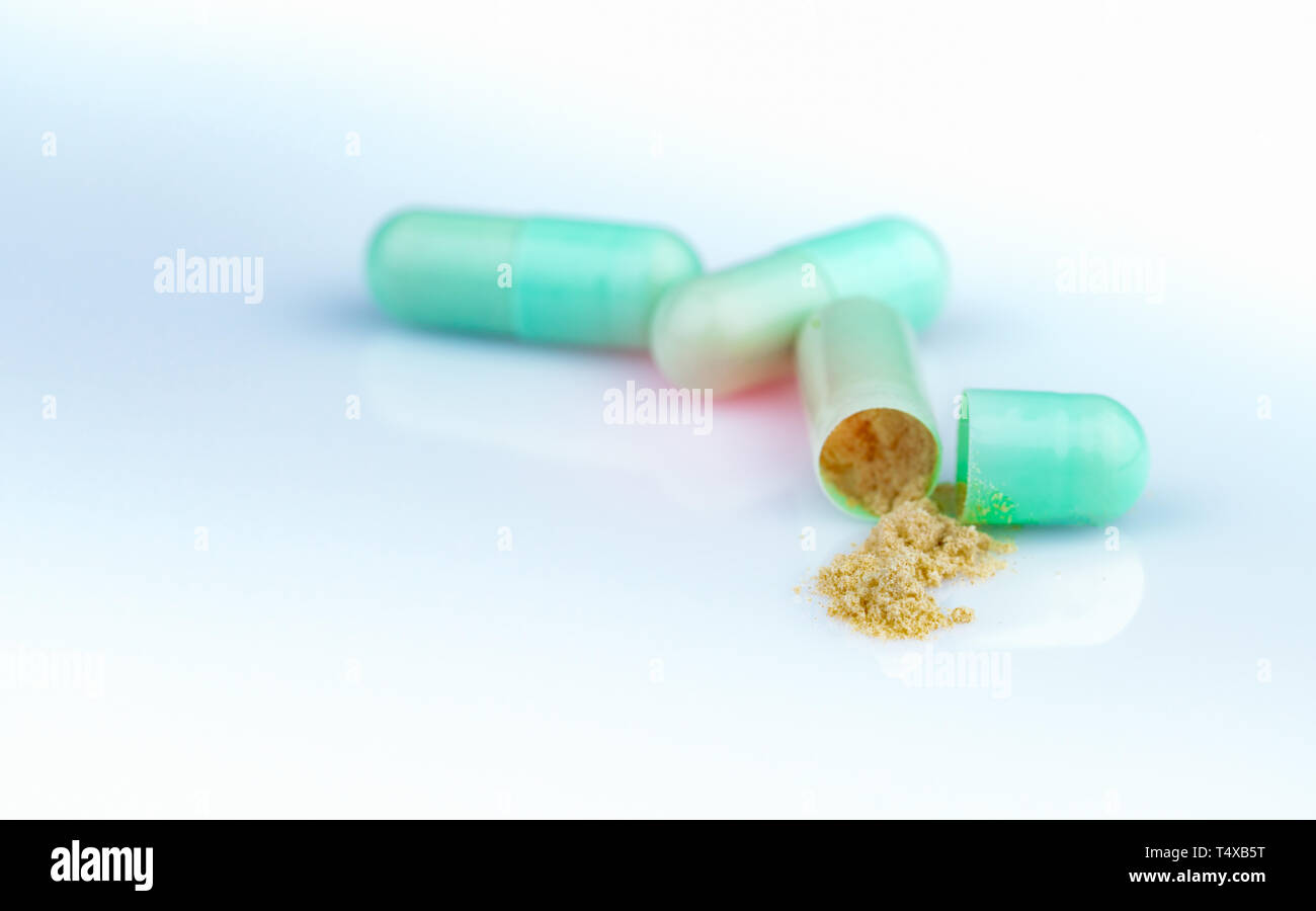 Group of green capsule and open one capsule to show yellow powder of herbal medicine on gradient background. Pharmaceutical product. Green capsule Stock Photo
