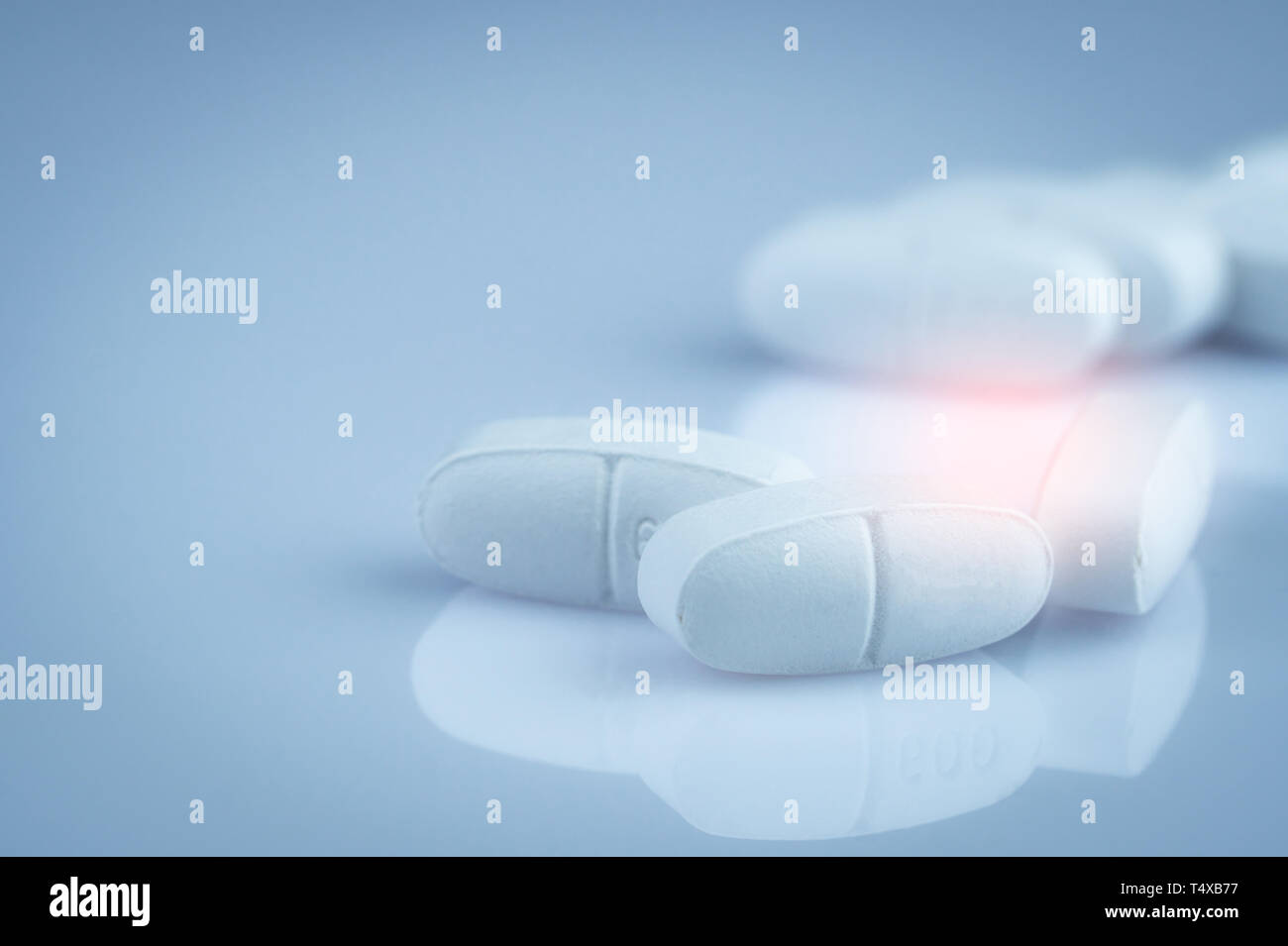 Pile of white oblong tablets pills on gradient background. Pharmaceutical industry. Pharmacy product. Global healthcare. Drug in pharmacy drugstore or Stock Photo