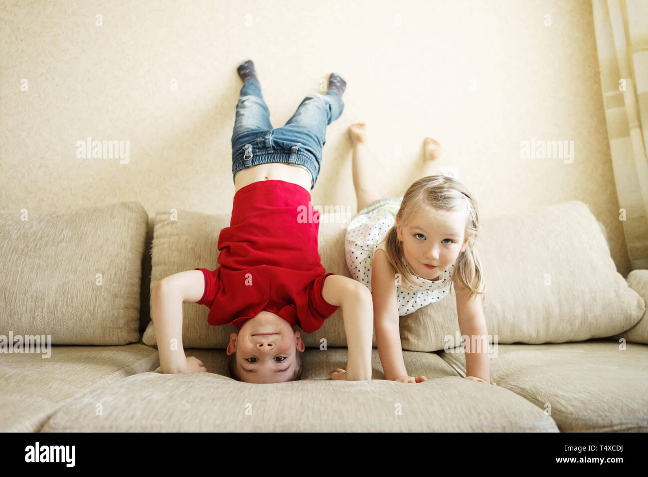 Brother and sister playing on the couch: the boy stands upside down. Stock Photo