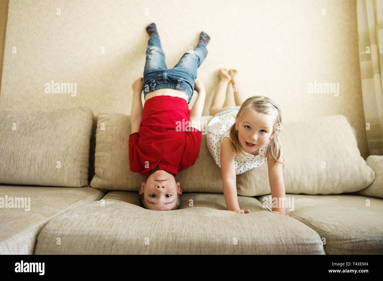 Brother and sister playing on the couch: the boy stands upside down Stock Photo