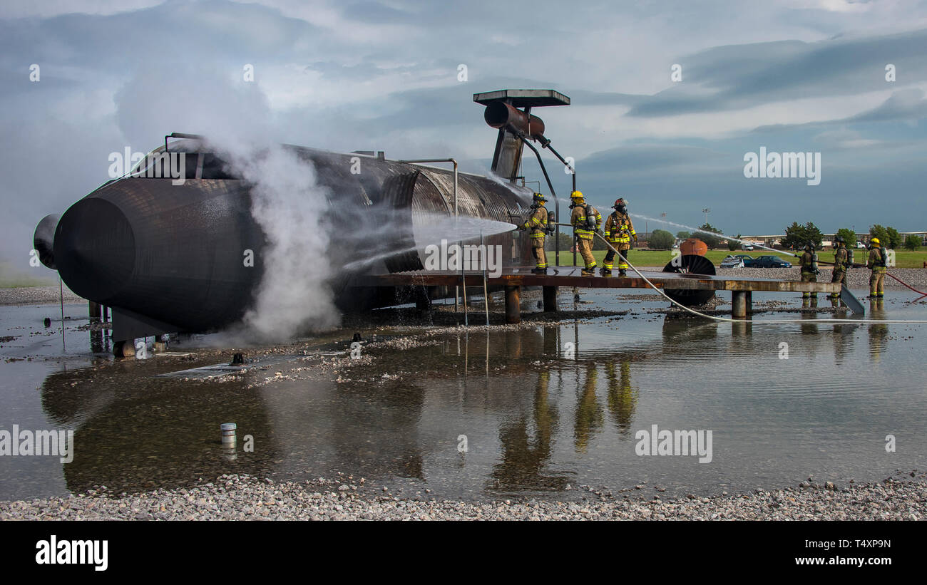 Firefighters spray water on a mock aircraft to cool it down after live-fire training at Sheppard Air Force Base, Texas, April 17, 2019. Crews from Sheppard, Wichita Falls, Texas, and Lawton, Oklahoma, converged on the training pit to hone their skills at attacking aircraft fires externally and internally. Sheppard, located on the north edge of Wichita Falls, is home to the 80th Flying Training Wing's Euro-NATO Joint Jet Pilot Training program, which uses the artillery range at Fort Sill near Lawton. (U.S. Air Force photo by John Ingle) Stock Photo