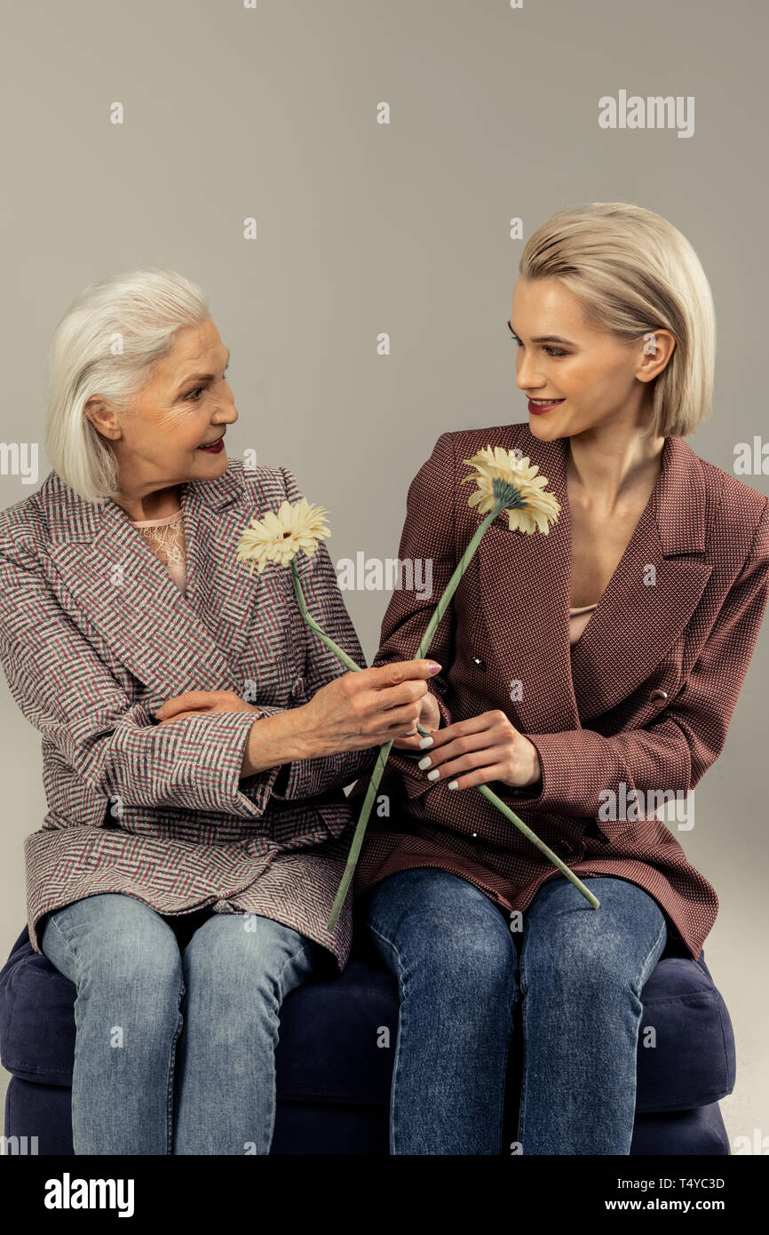 Positive delighted women giving each other flowers Stock Photo