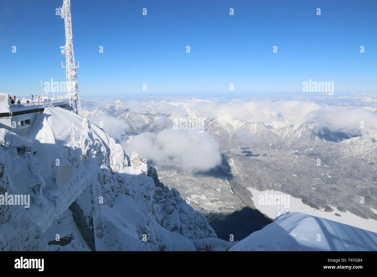 Zugspitze: Rechts der vereiste Eibsee, links ein sendemast auf dem Gipfel. Im Tal schweben dunkle Wolken und werfen Schattem auf die Berge. Stock Photo