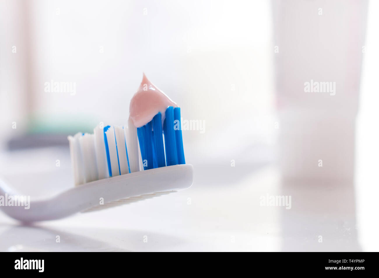 Toothbrush with pink toothpaste on the bathroom sink with dispenser in
