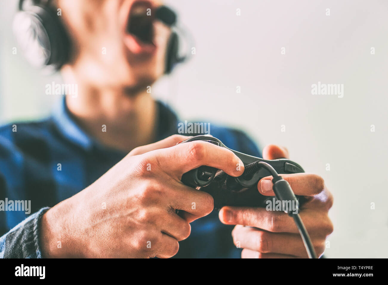 Young man having fun playing video games online using headphones and microphone - Close up male hands gamer holding a joystick - Vintage filter Stock Photo