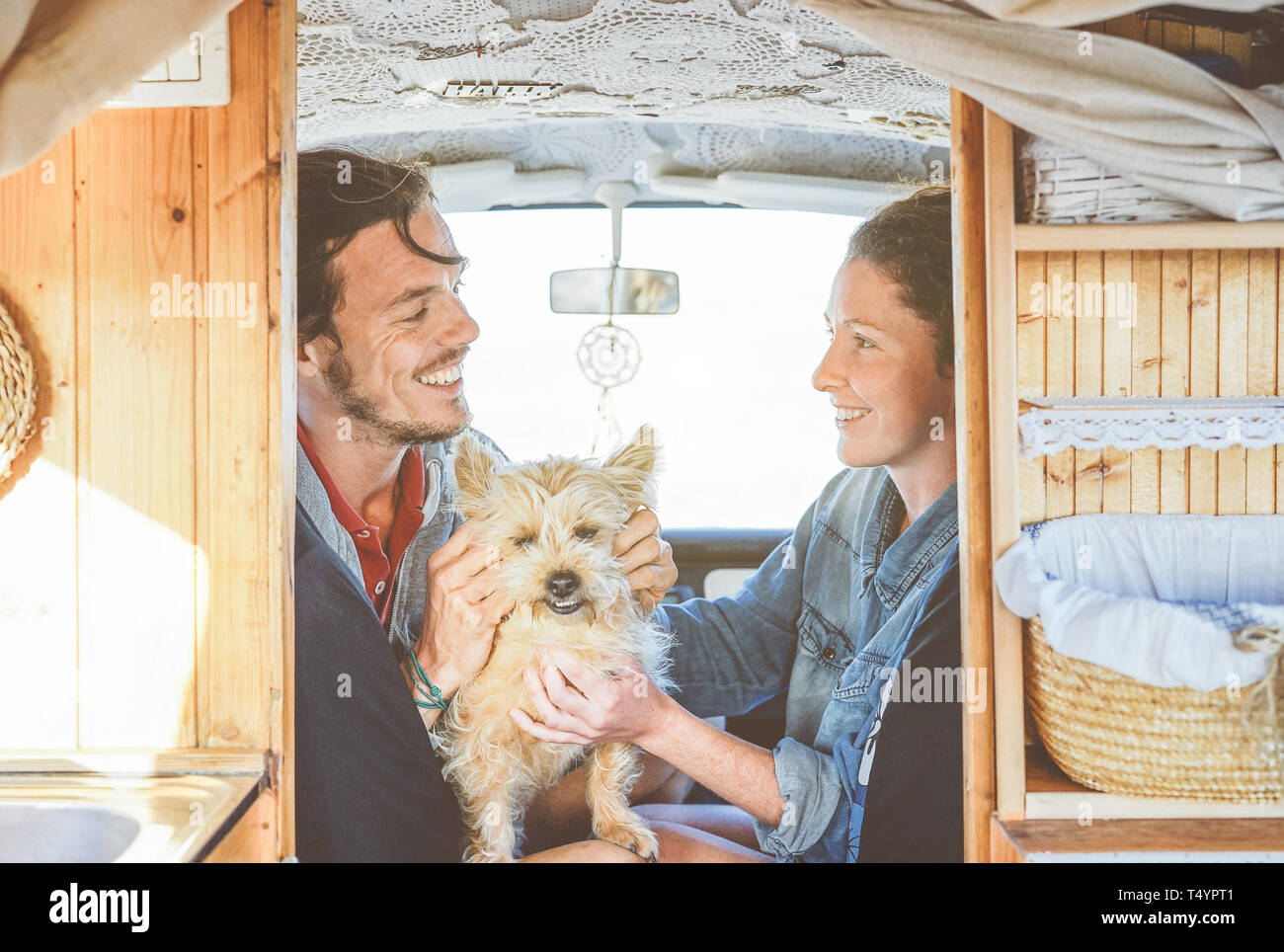 Happy couple cuddling their dog inside a mini van - Young people getting ready for a road trip having fun together with their pet Stock Photo