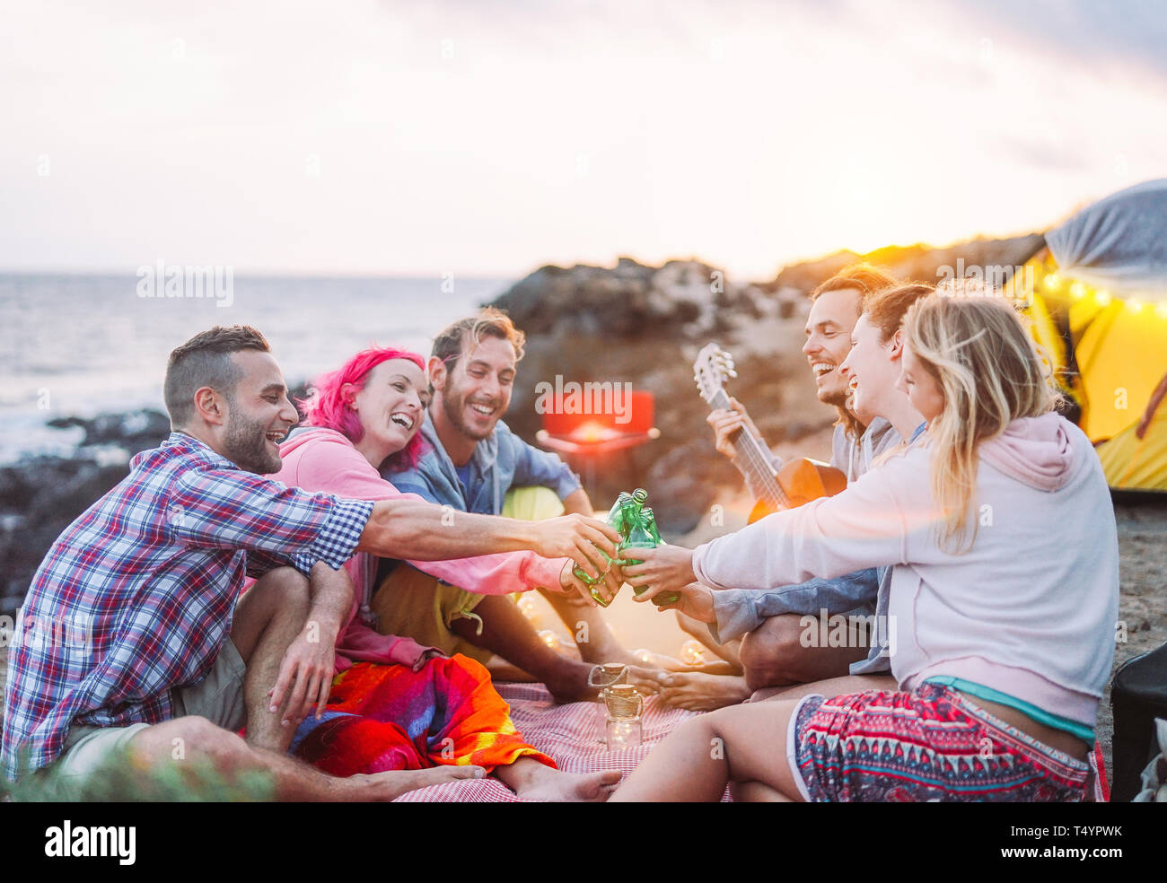 Group of friends cheering with beers outdoor - Happy people camping with tent and making a barbecue having fun toasting bottles of beer Stock Photo