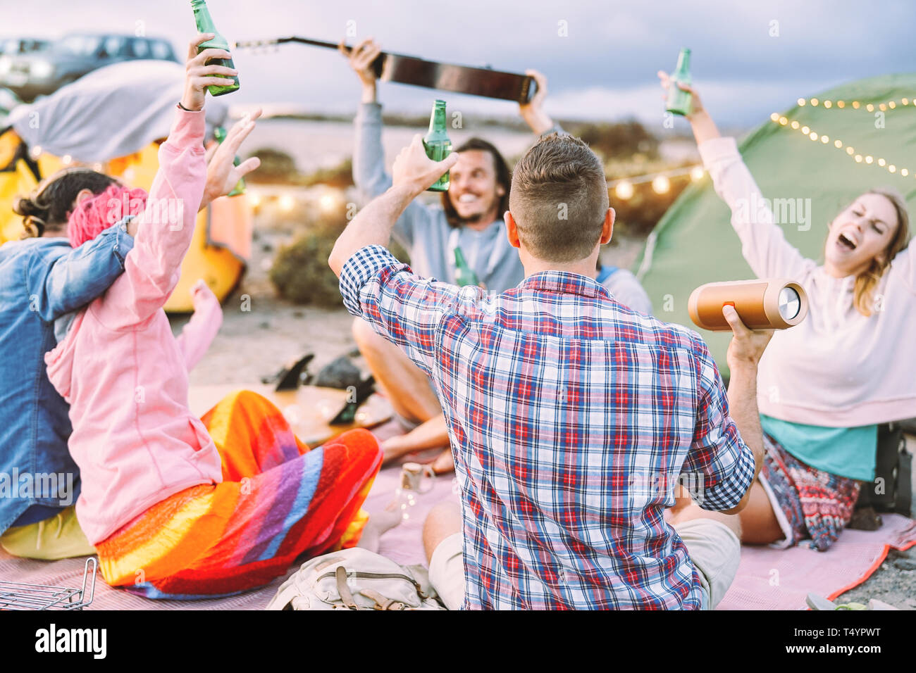 Happy friends making party drinking beers and playing music while camping with tents outdoor - Young people having fun and laughing together Stock Photo