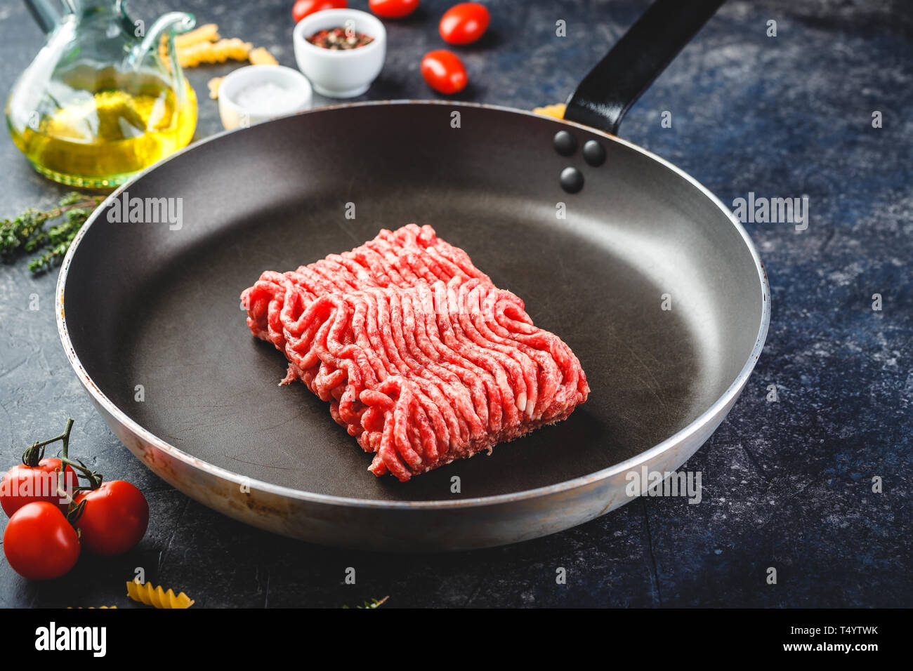 Fresh raw minced beef in frying pan and ingredients over dark background. Stock Photo