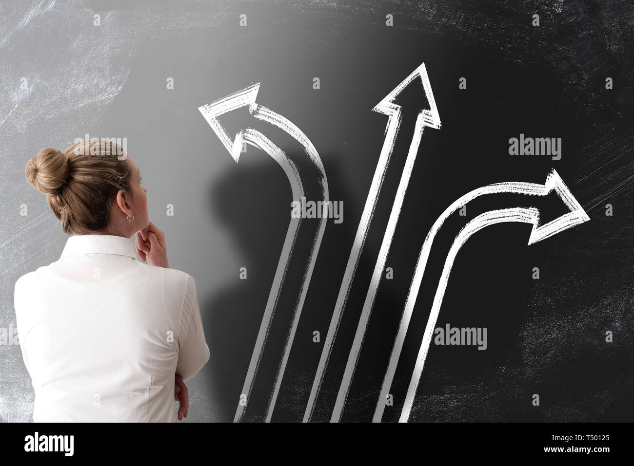 taking the right way and making decisions concept with rear view of woman looking at chalkboard with arrows pointing in different directions Stock Photo