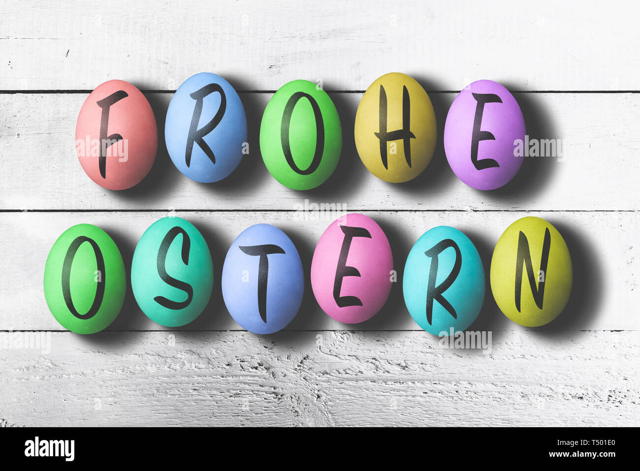 FROHE OSTERN, German for happy easter, written on colored easter eggs against rustic white wooden table Stock Photo