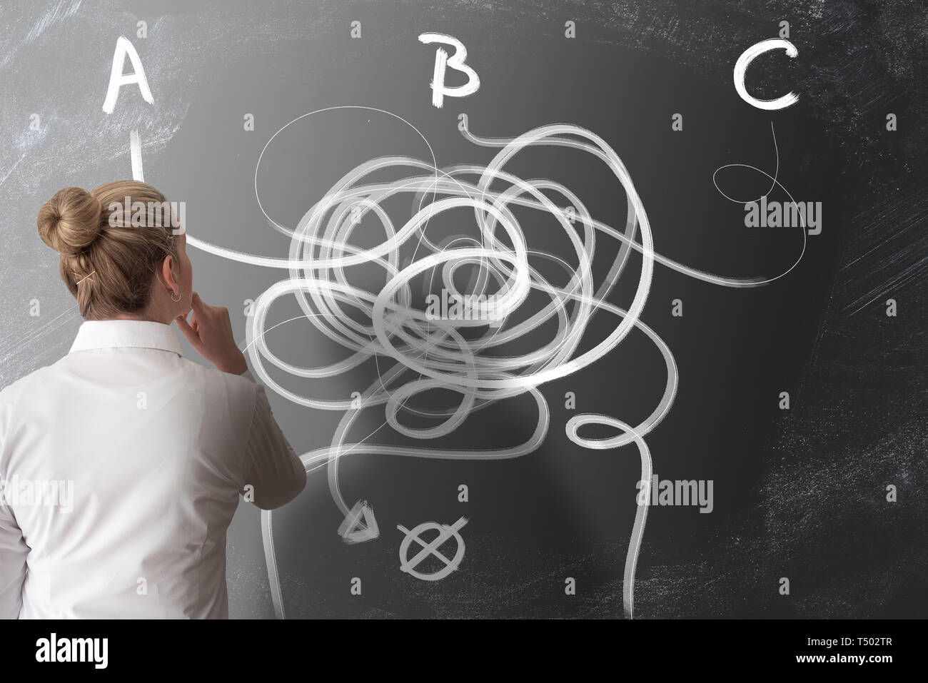 finding the right way and making decisions concept with rear view of woman looking at chalkboard with twisted lines pointing in different directions Stock Photo