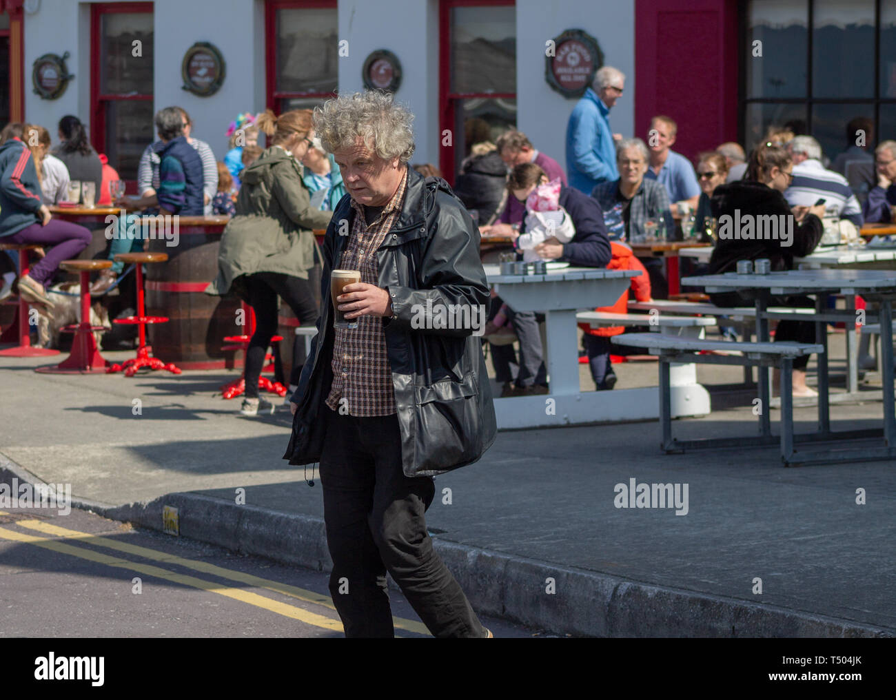 Man crossing the road holding a pint of Irish stout beer on a summer day. Stock Photo