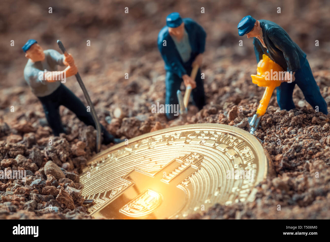 macro miner figurines digging ground to uncover big shiny bitcoin Stock Photo