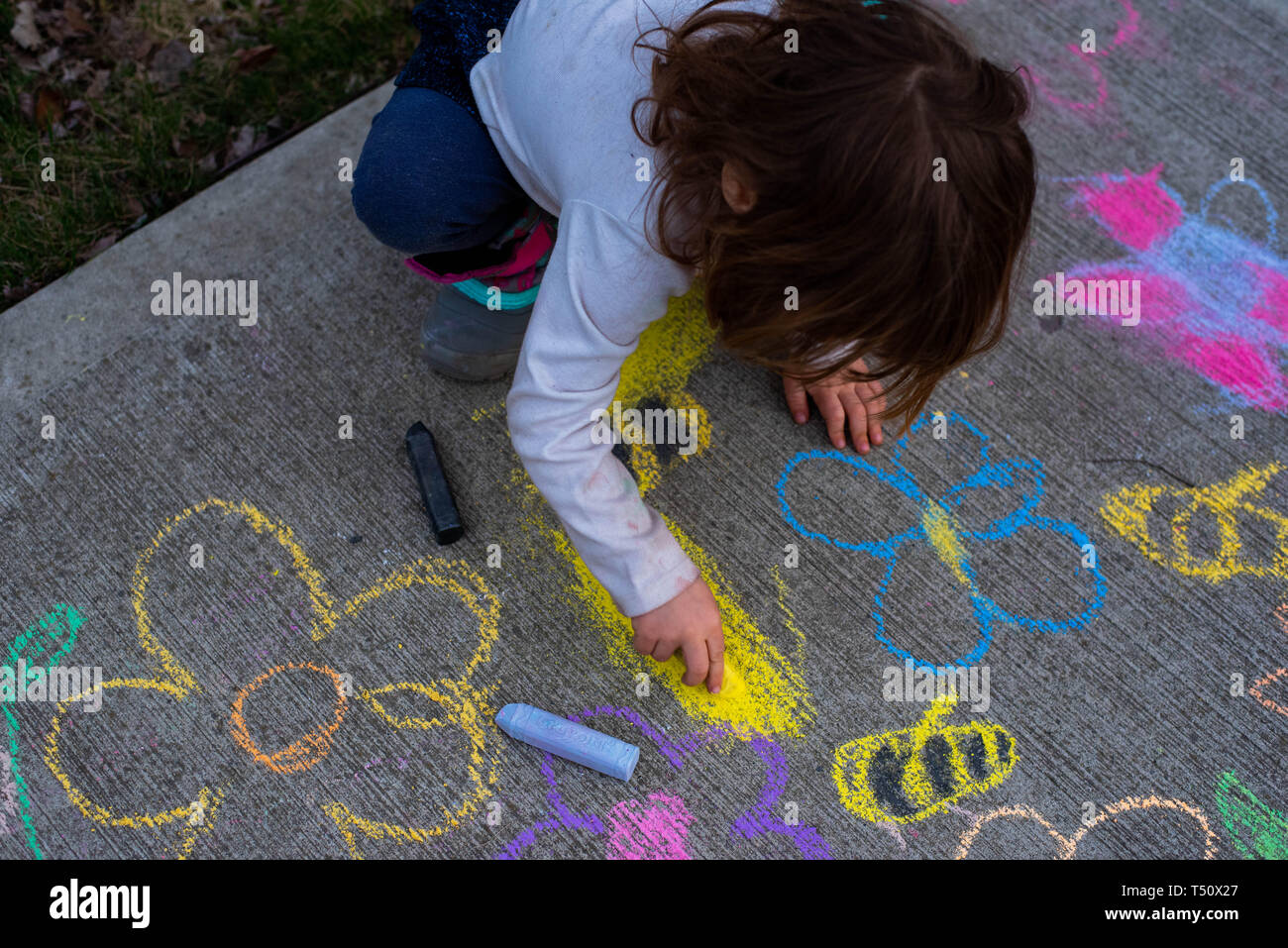 A young girl drawing with sidewalk chalk on the sidewalk in summer. Stock Photo