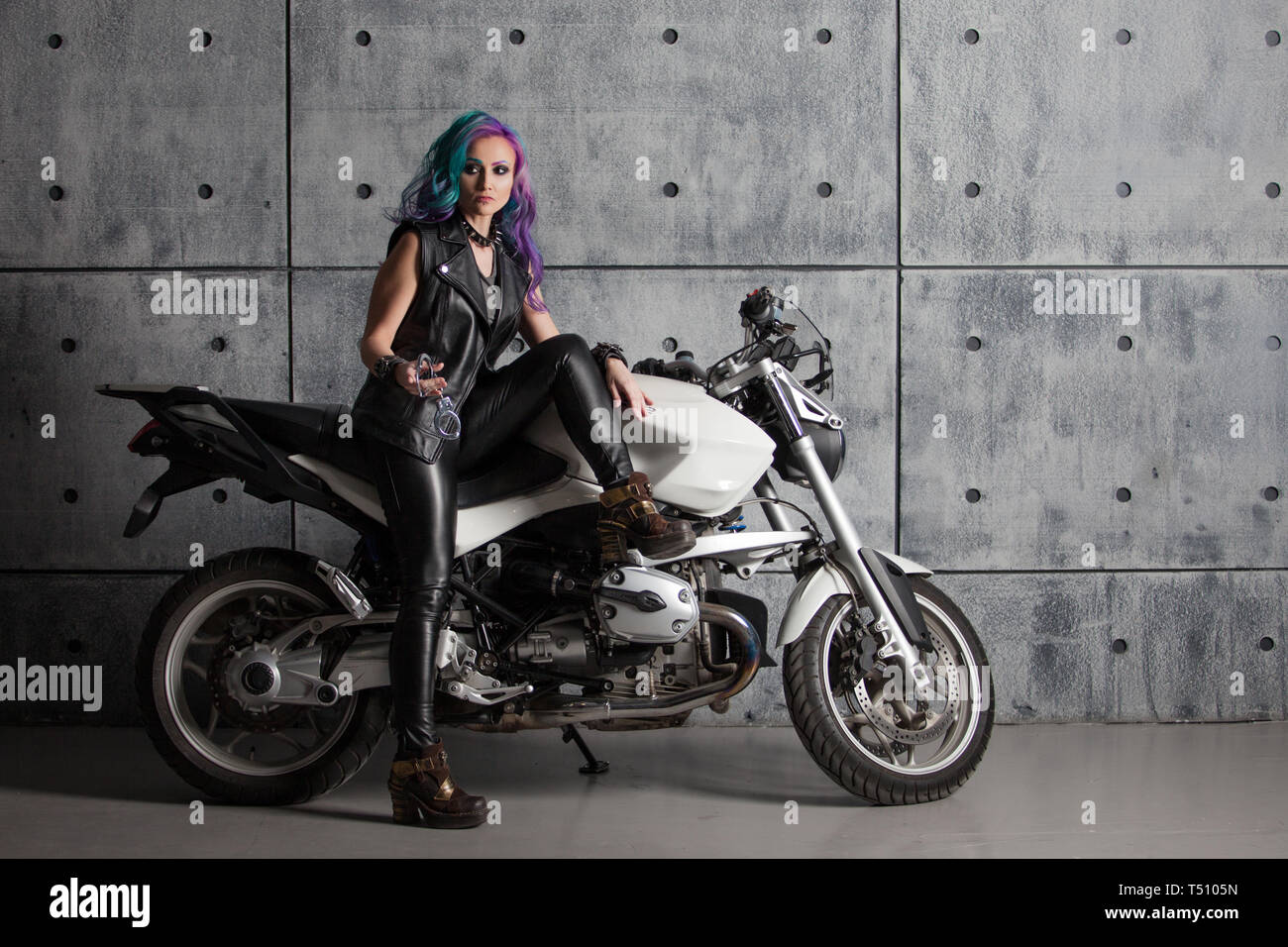 Biker chick in front of motorcycle. Beautiful and pert young woman in leather clothes and with colored hair. Stock Photo