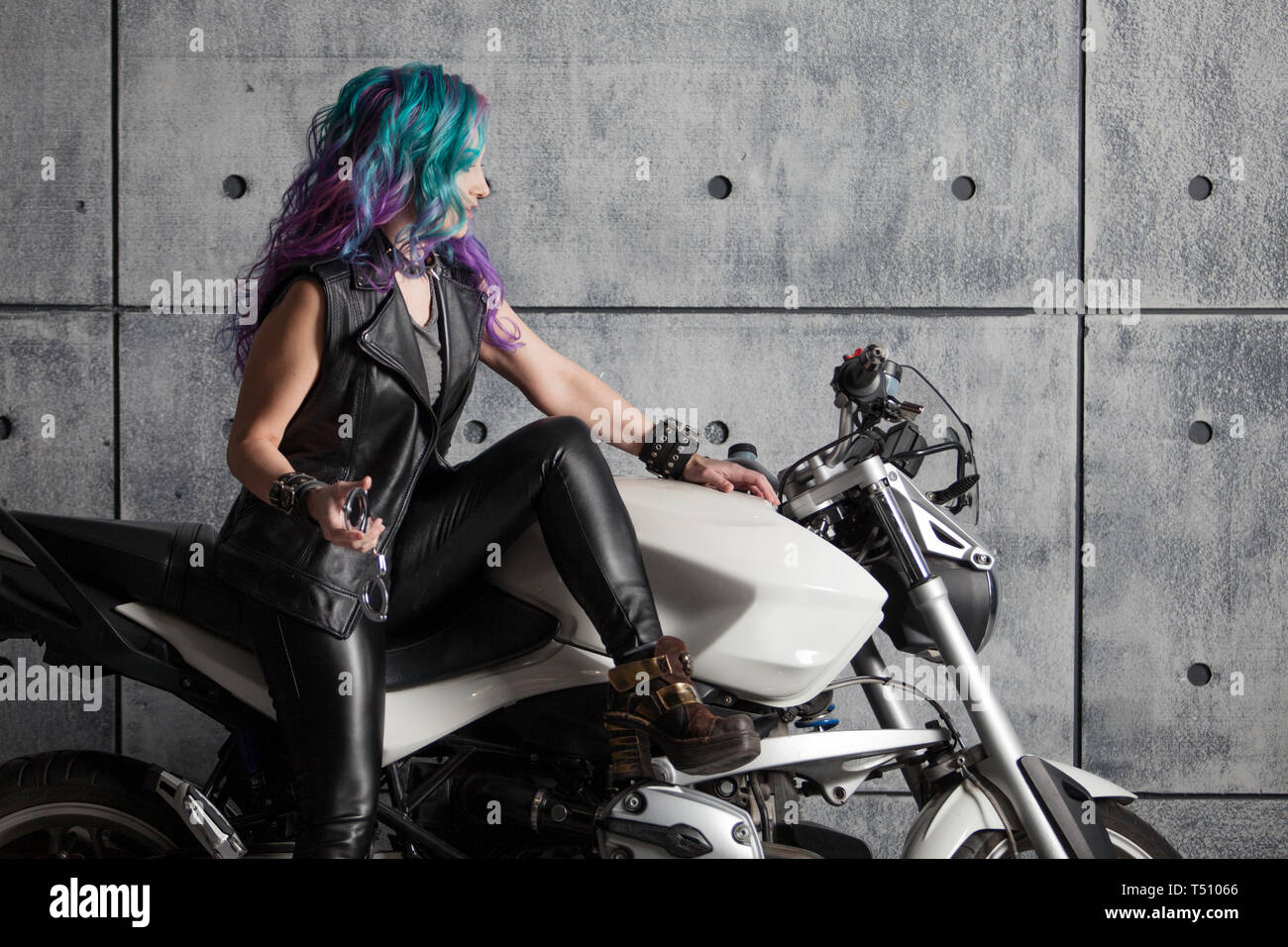 Biker chick in front of motorcycle. Beautiful and pert young woman in leather clothes and with colored hair. Stock Photo