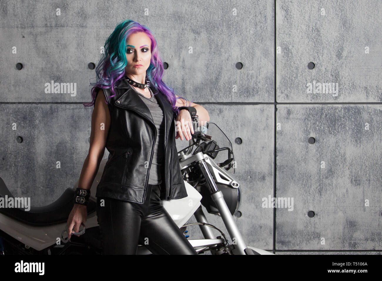 Biker chick in front of motorcycle. Beautiful and pert young woman in leather clothes and with colored hair. Stock Photo