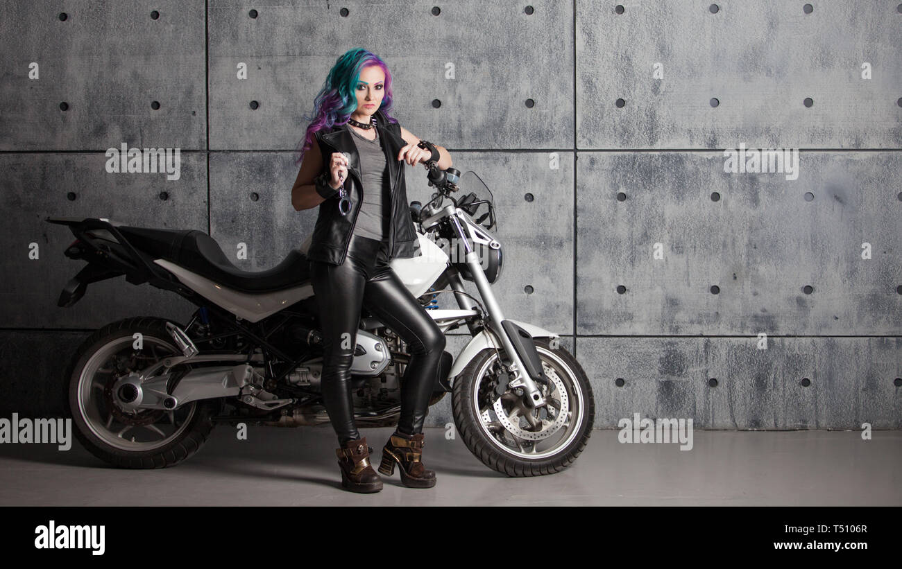 Biker chick in front of motorcycle. Beautiful and pert young woman in leather clothes and with colored hair. Stock Photo