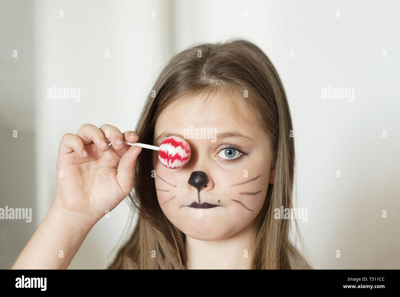 blonde girl with a make-up imitating a cat holds in her hand a chupa chups. Stock Photo