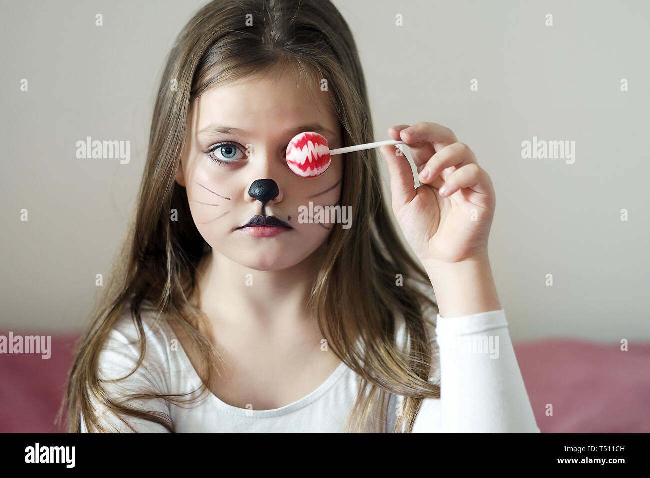 blonde girl with a make-up imitating a cat holds in her hand a chupa chups. Stock Photo