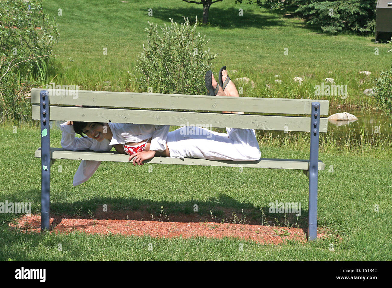 Pretty dark haired woman lying on a wooden  park bench. Stock Photo