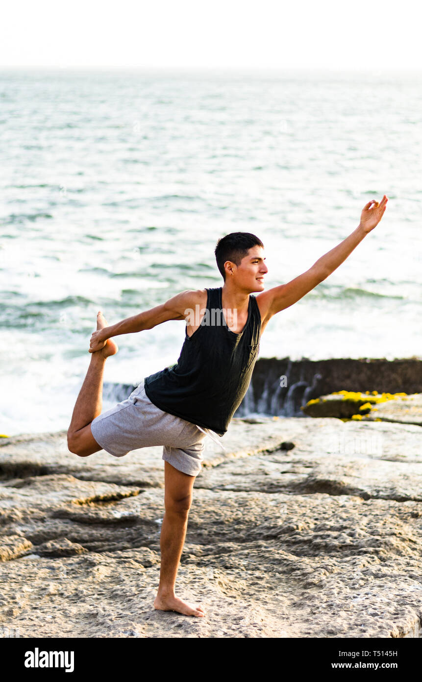 Healthy man practicing yoga. Stretching in natural position in Natarajasana, beautiful sea landscape, sunset, nature, concept for exercise, health care Stock Photo