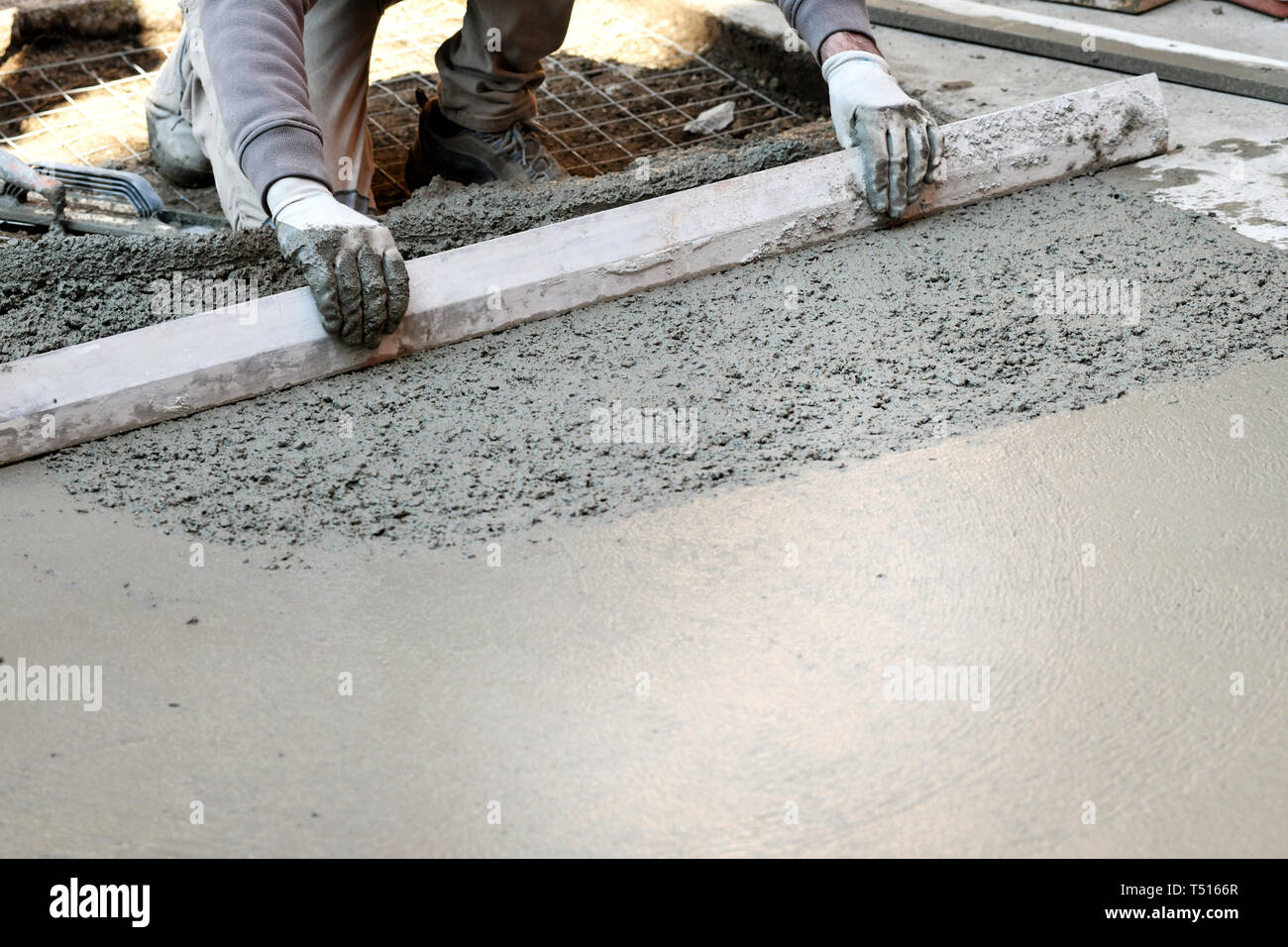 Worker spreading and flattening cement mortar with hand tool, making concrete floor Stock Photo