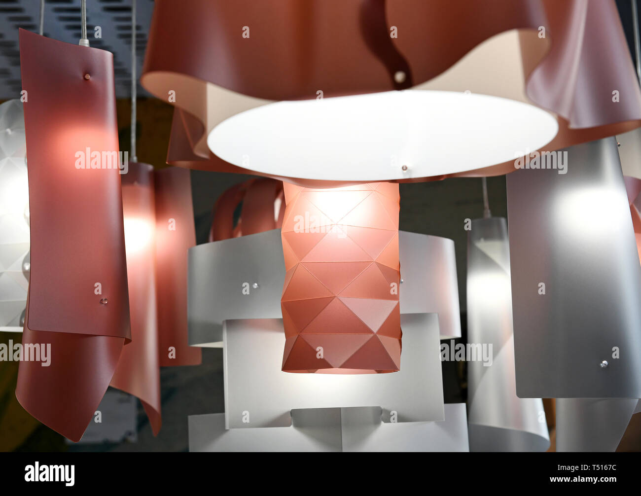 Modern plastic chandeliers of red and silver colors with geometrical shape design and glowing lamps, hanging on white wires. Viewed in close-up from l Stock Photo