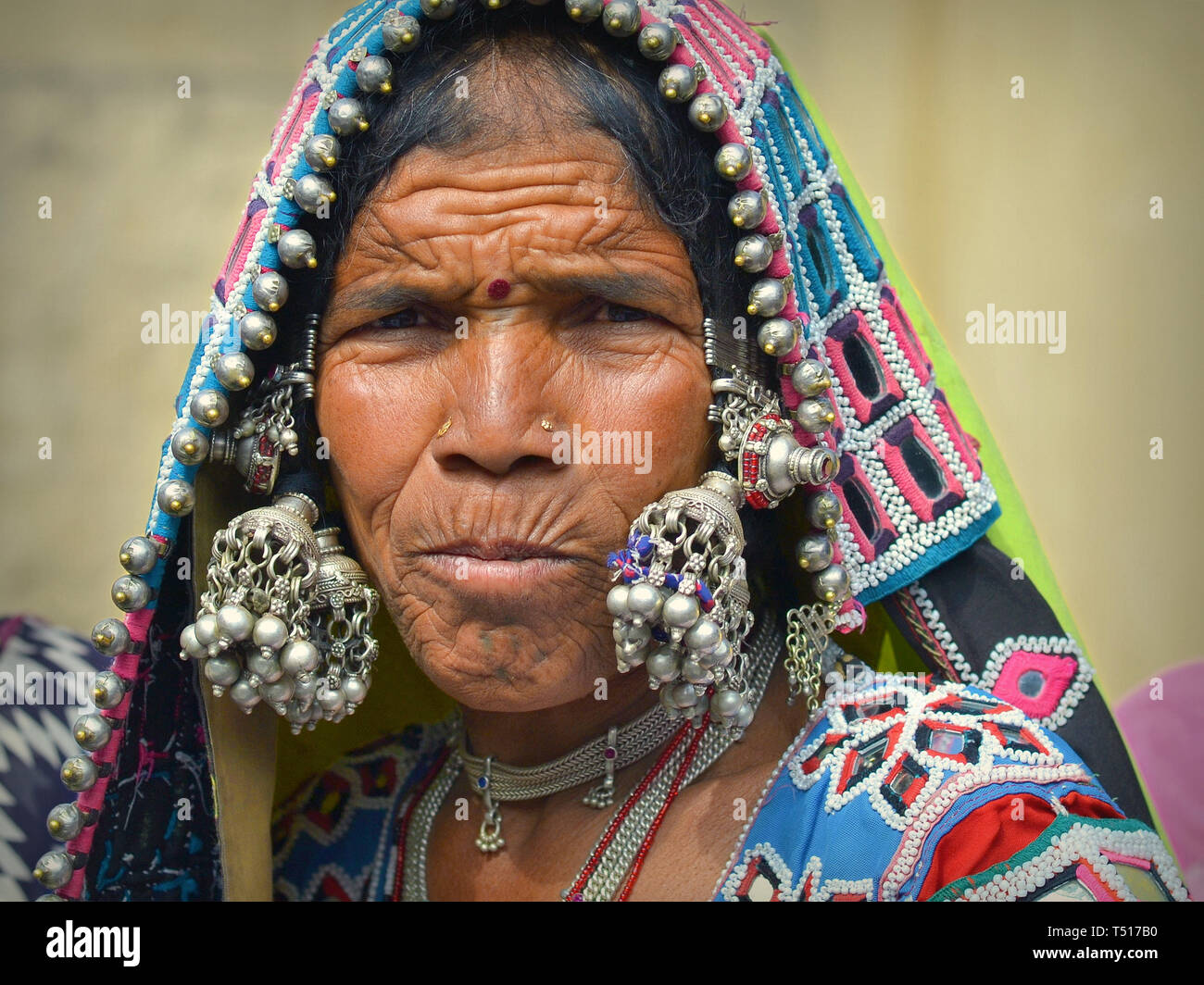 Elderly Indian Banjara tribal woman wears her intricately embroidered, colourful tribal garment and headscarf with innumerable silver balls and bells. Stock Photo