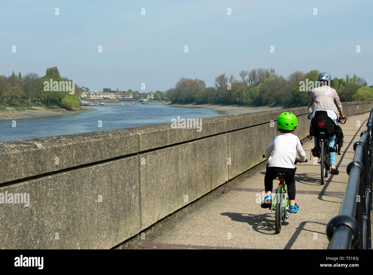 woman and young boy cycle on the footway beside the river thames in barnes, london, england Stock Photo
