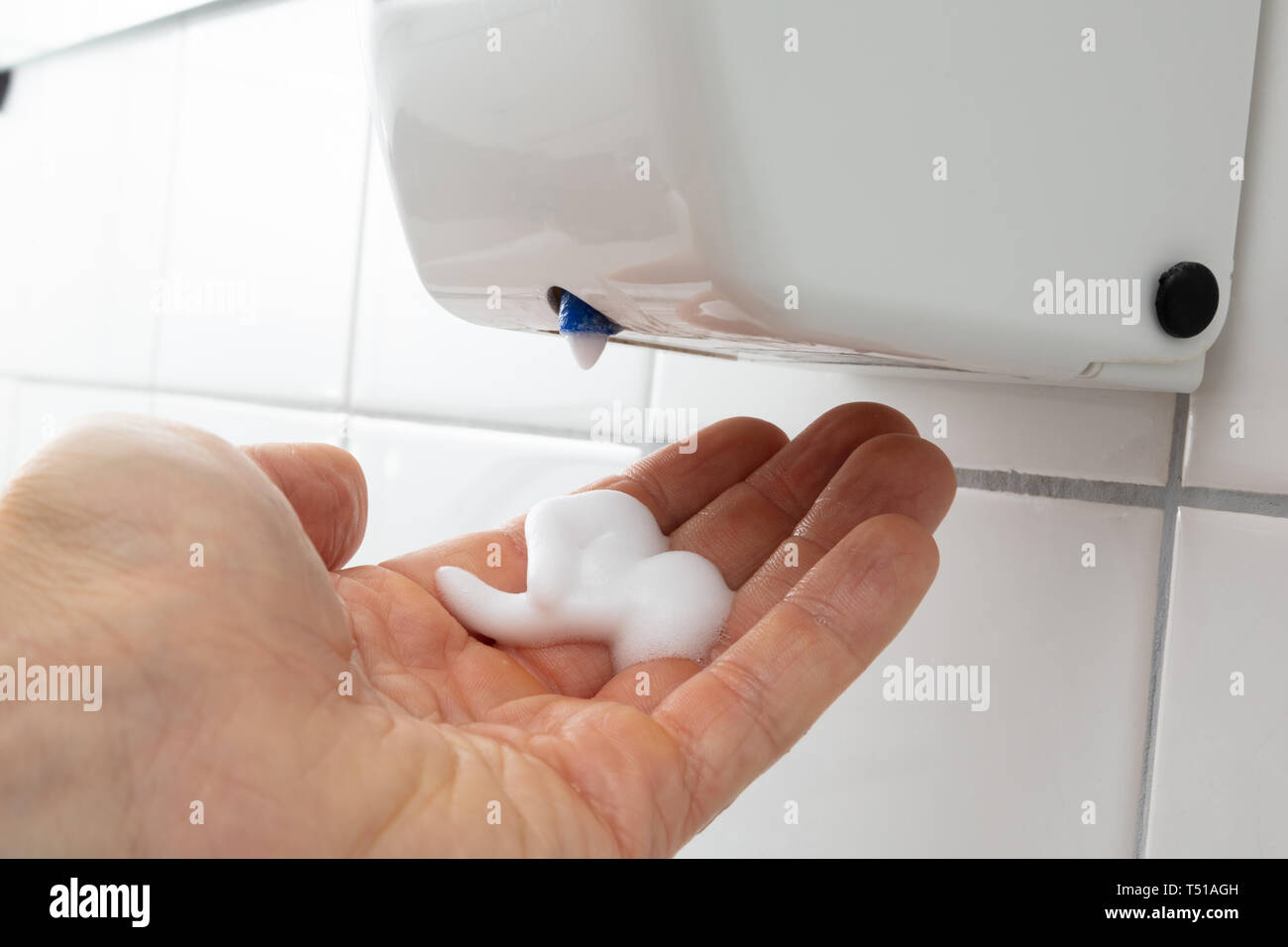 Close-up Of Person's Hand With Liquid Soap Dispenser On Tiled Wall Stock Photo