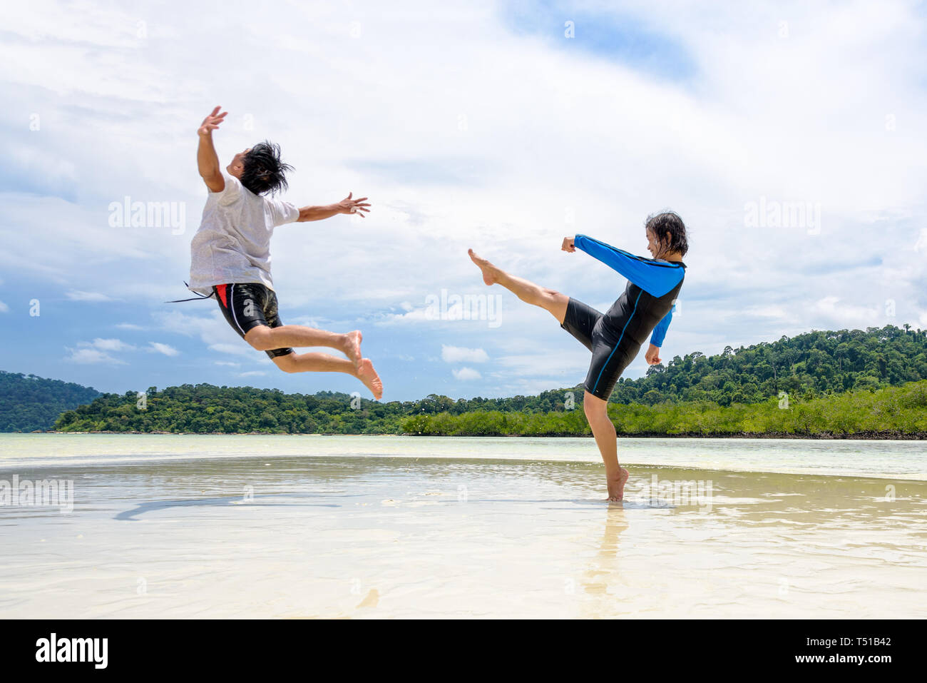 Happy asian couple play fun activity together woman show the teasing position, kicking a man to bounce far away on the beach of Ko Ra Wi near Ko Lipe  Stock Photo